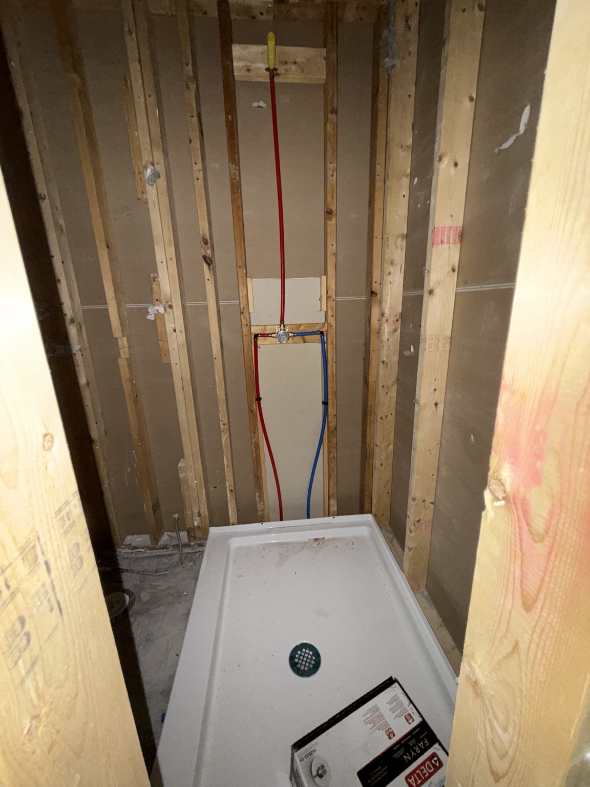 Red and blue PEX water lines routed to a shower valve during a residential rough-in by AHVEE
